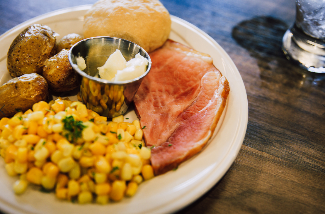 A plate of food featuring ham, corn, bread, and butter.
