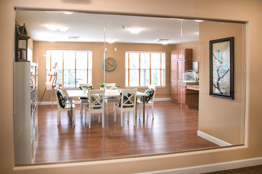 A spacious dining area with a modern kitchen visible in the background, featuring large windows that allow ample natural light.