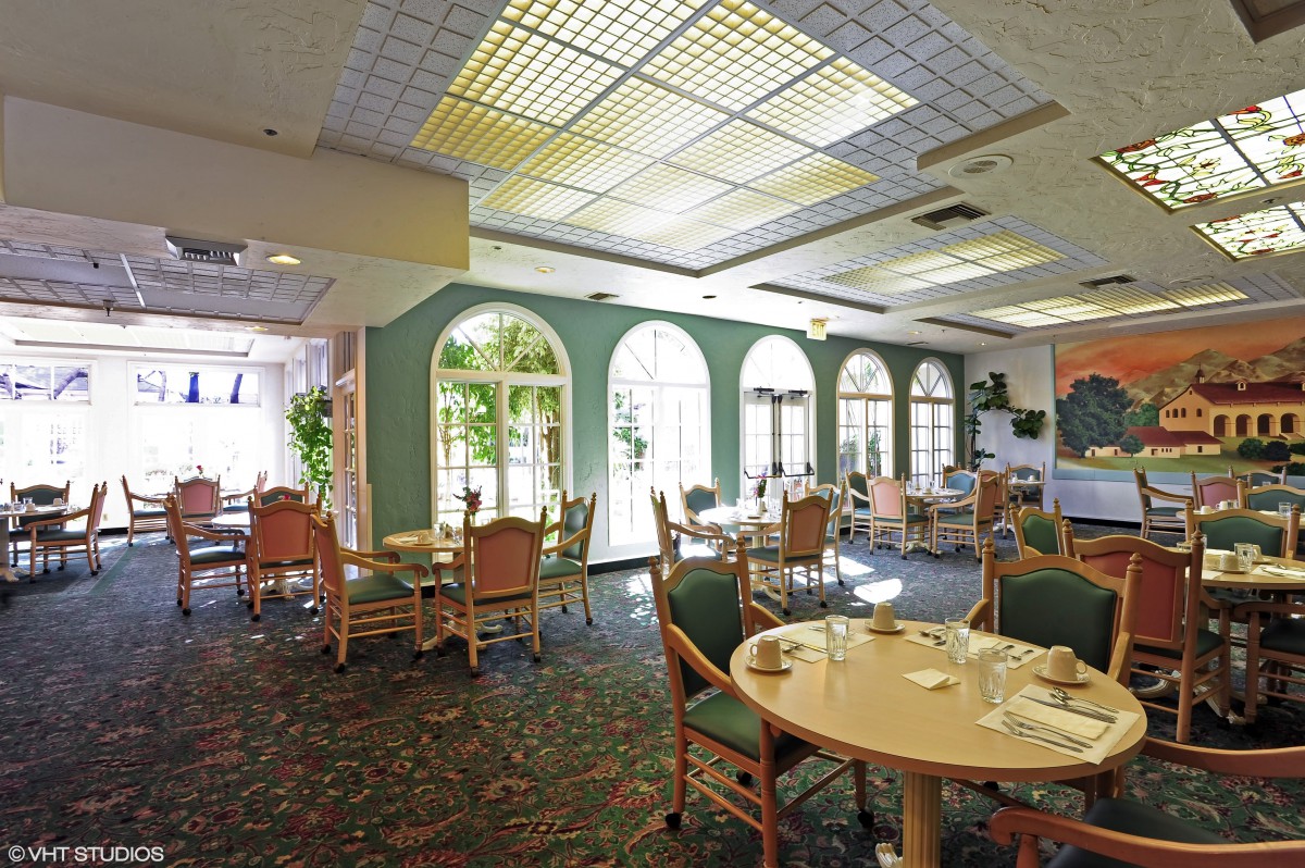 A well-lit dining area with tables and chairs arranged near large windows.
