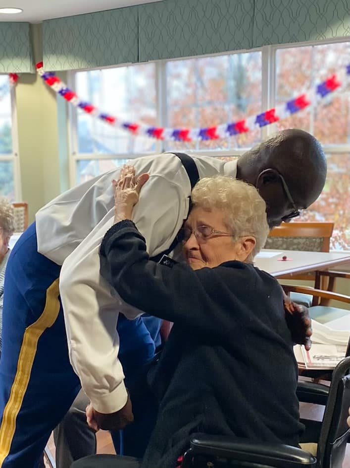 An elderly woman embraces a man warmly inside a decorated room.