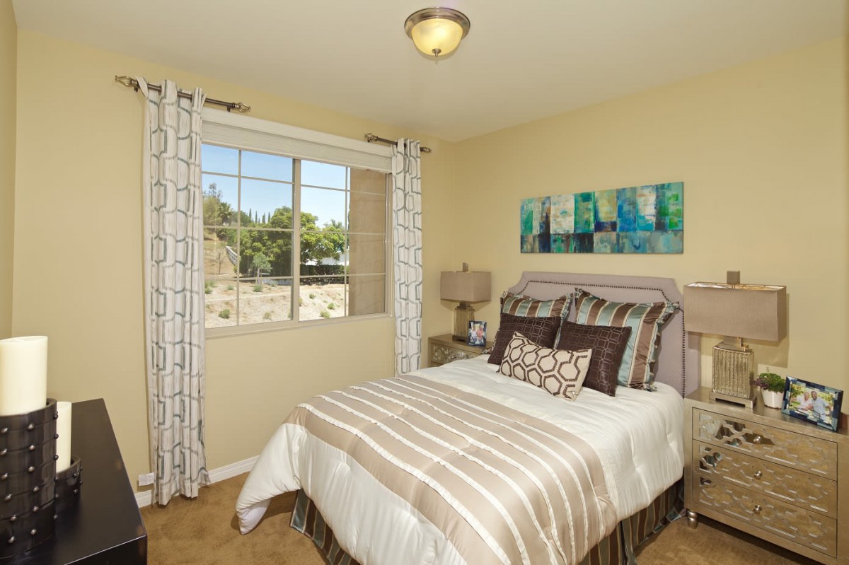 A cozy bedroom with a neatly made bed, decorative pillows, and a window letting in natural light.