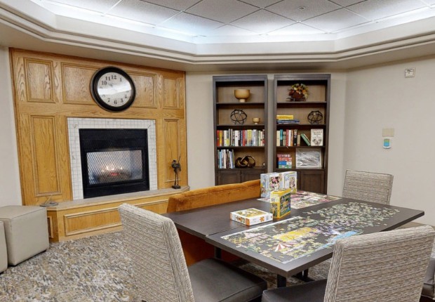 A cozy library room with a fireplace, bookshelves, and a table set up for puzzles.