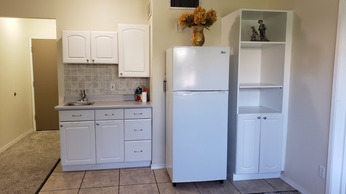A kitchen with white cabinets, a white fridge, and tiled flooring.