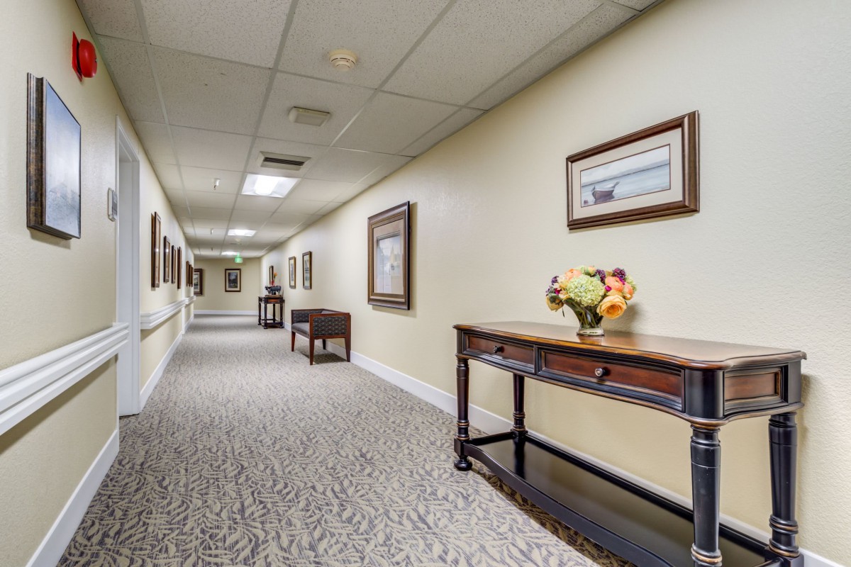 A well-lit hallway with decorative tables and framed artwork on the walls.
