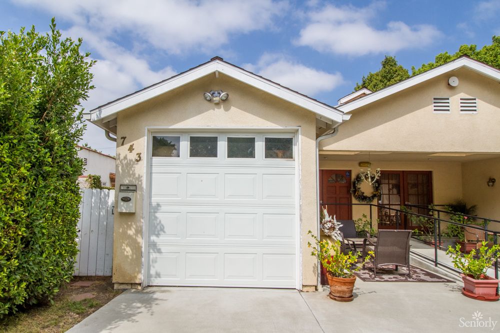 A single-car garage of a suburban house with a driveway and potted plants in the front yard.