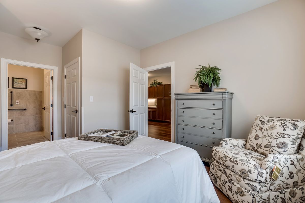 A cozy bedroom featuring a bed, dresser, and upholstered chair with a decorative plant on top of the dresser.