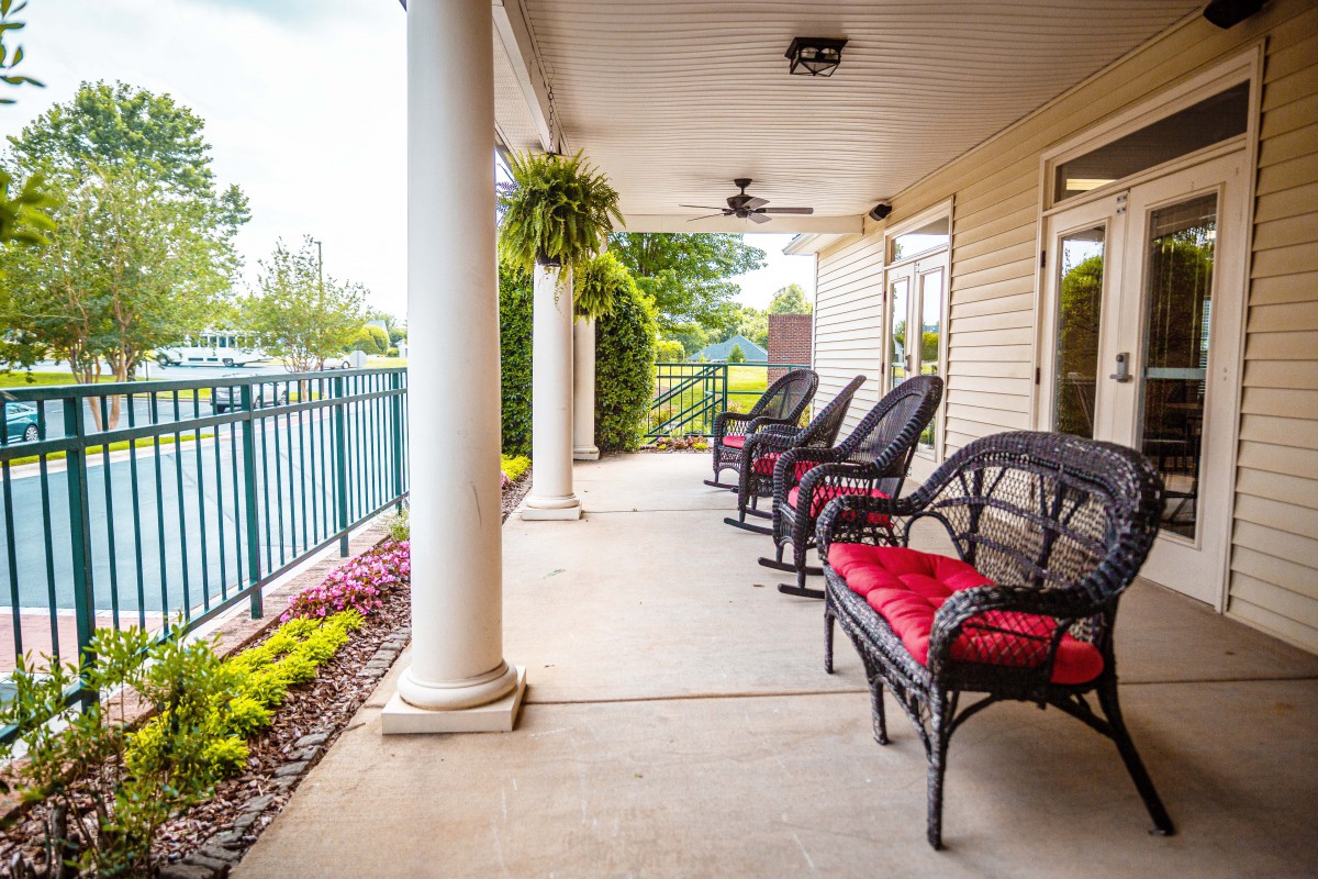 A cozy porch with chairs featuring red cushions, surrounded by plants and overlooking a peaceful outdoor space.