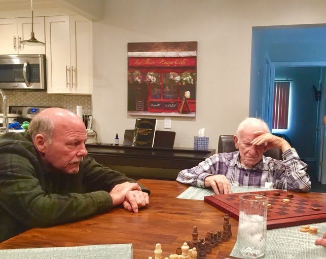 Two elderly men engaged in a game of chess at a kitchen table.