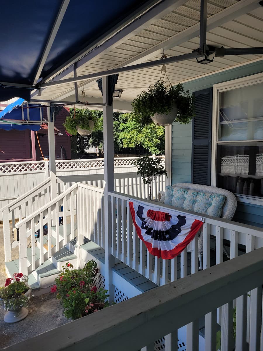 A cozy porch decorated with patriotic bunting and lush hanging plants, perfect for a sunny day relaxation.