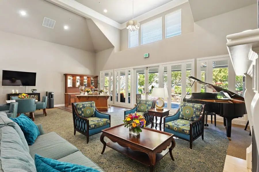 A spacious living room featuring comfortable seating, a piano, and large windows.