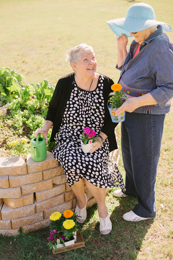 Two women enjoy their time in the garden, surrounded by colorful flowers and greenery.