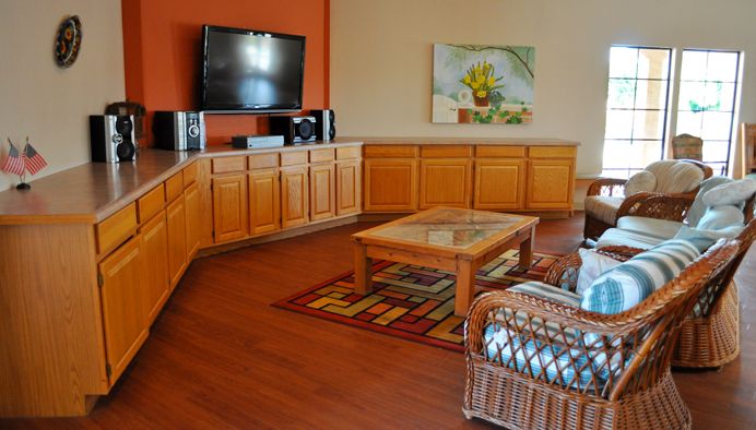 A cozy living room featuring a large television, wooden cabinets, and a coffee table on hardwood floors.