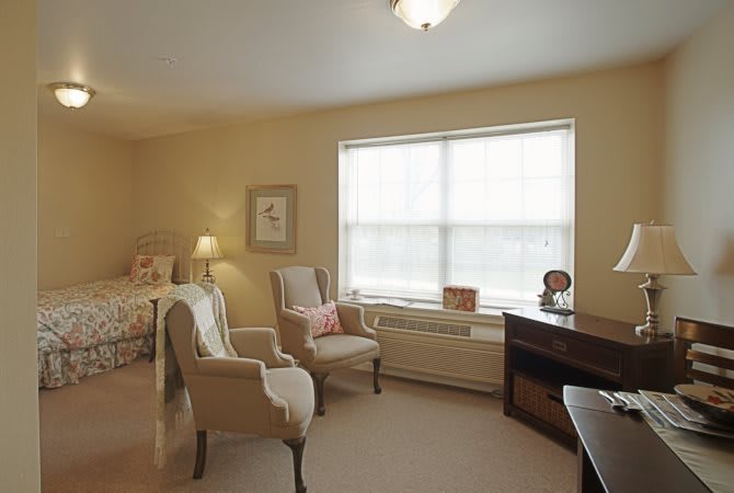 A cozy bedroom with chairs, a bed, and a window letting in natural light.