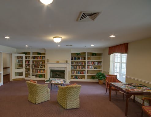 A cozy library room with bookshelves, a fireplace, and comfortable seating.
