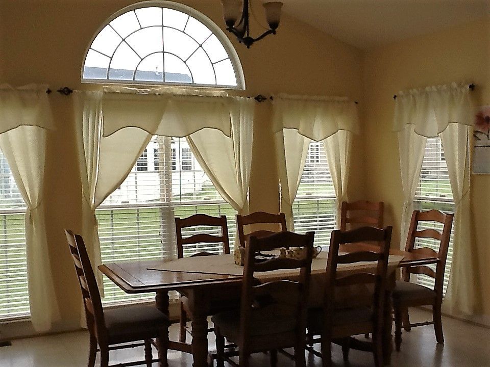 A cozy dining room with a wooden table and chairs, featuring large windows with curtains.