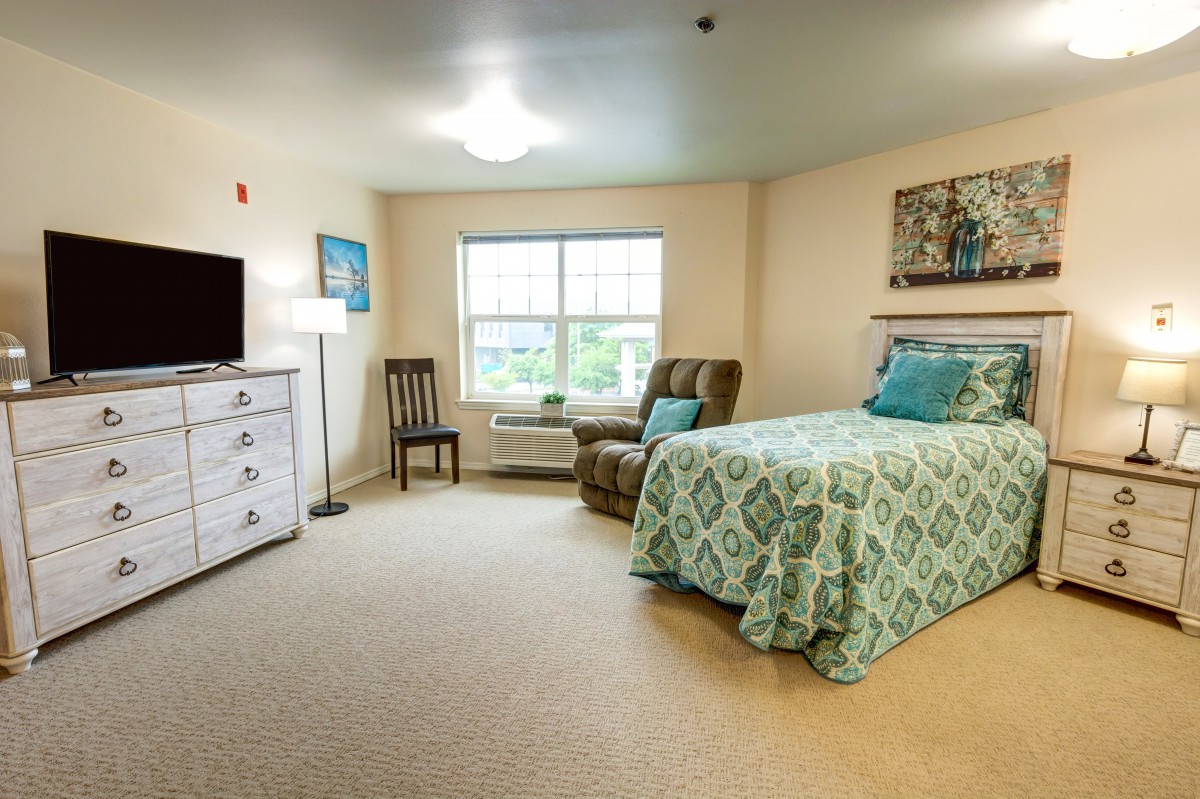 A cozy bedroom interior with a neatly made bed, armchair, and television.