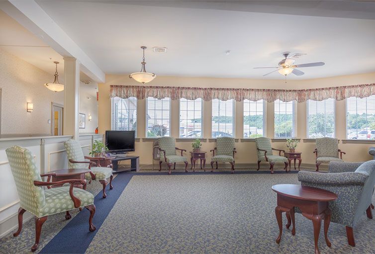 A spacious living room with traditional decor, featuring a seating area, large windows, and a television.