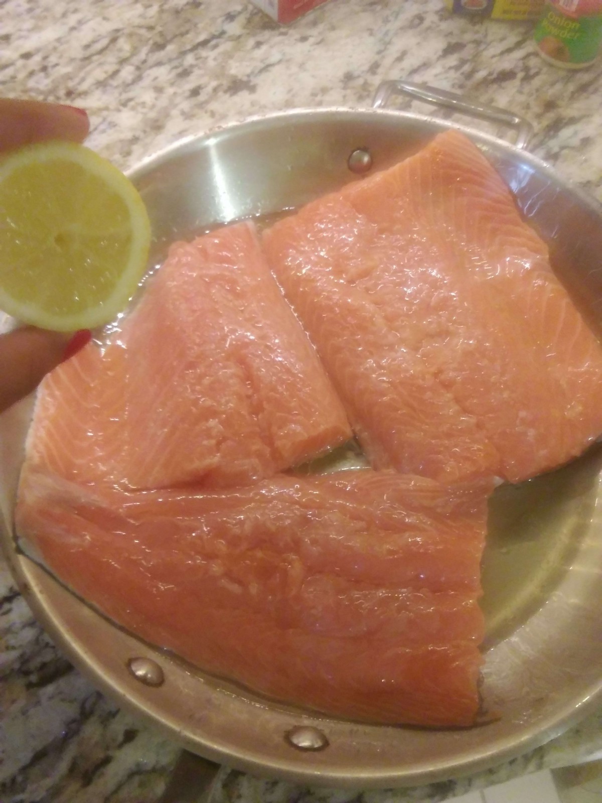 Preparing salmon fillets with a slice of lemon in a pan.