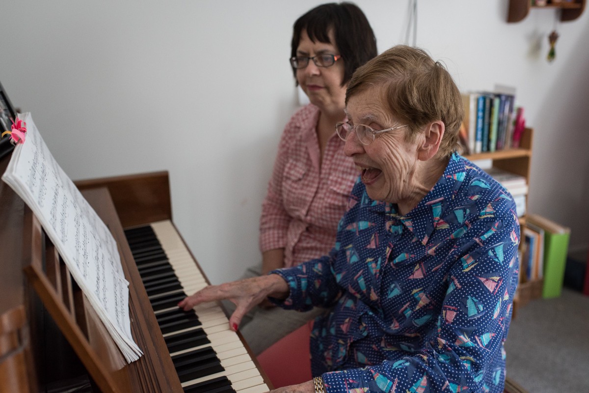 Two elderly women enjoying playing the piano together indoors.