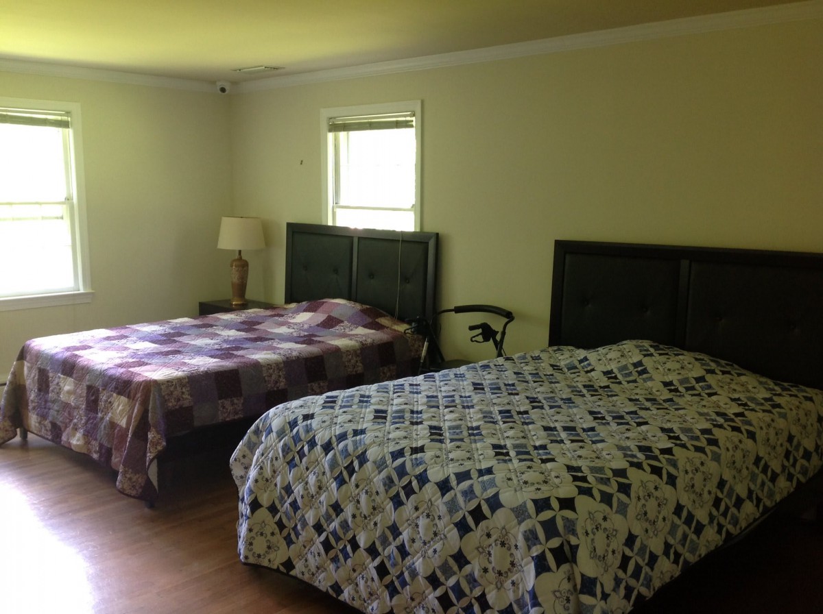 A cozy bedroom with two beds adorned with patterned quilts, a small window, and a lamp.