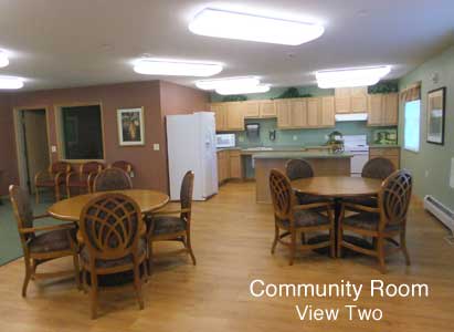 A community room featuring a kitchen area with tables and chairs.