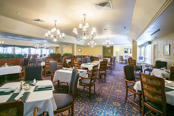 An elegant dining room with neatly arranged tables, chandeliers, and upholstered chairs.