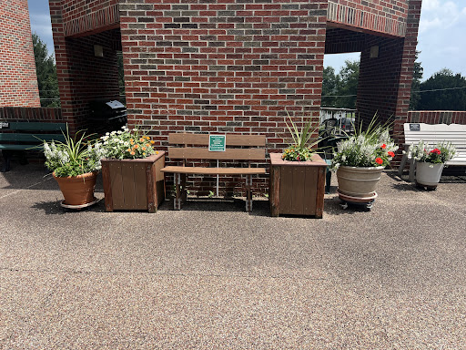 A cozy outdoor seating area featuring a wooden bench surrounded by lush planters against a brick wall.