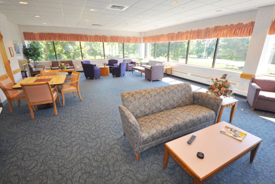 A spacious lounge with sofas, tables, and chairs, featuring large windows.