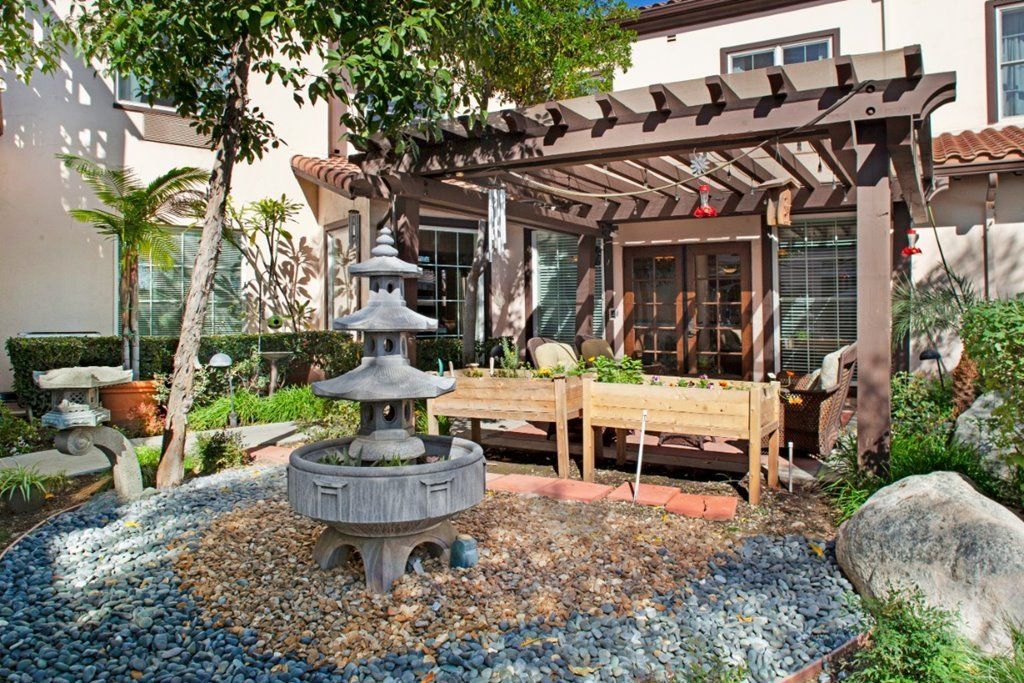 A beautifully landscaped garden with a fountain and pergola-covered patio area.