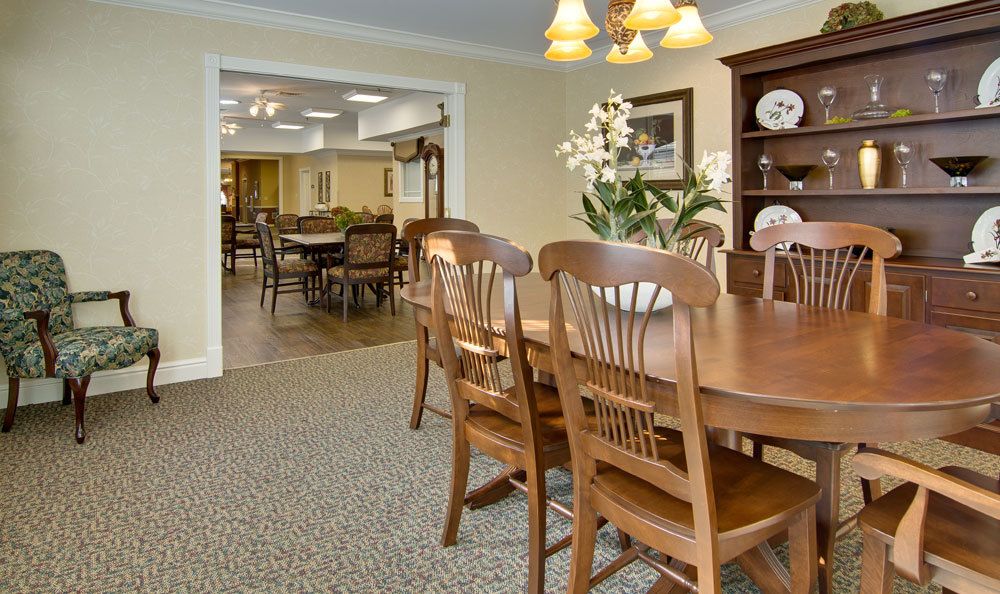 A cozy dining room with a wooden table and chairs, decorated with flowers and china plates.