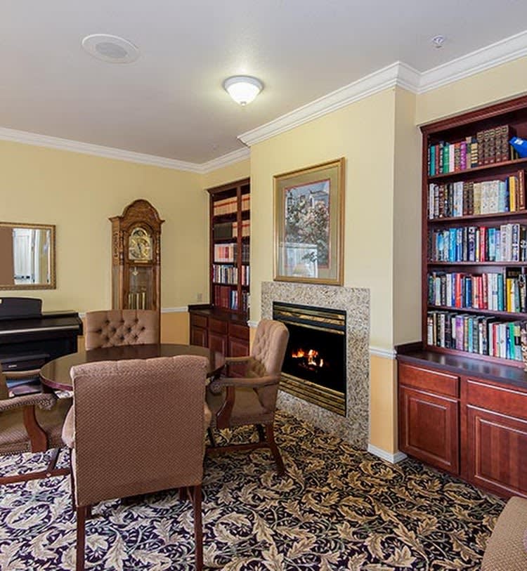 Cozy library room with a fireplace, surrounded by bookshelves and furnished with comfortable chairs and a piano.