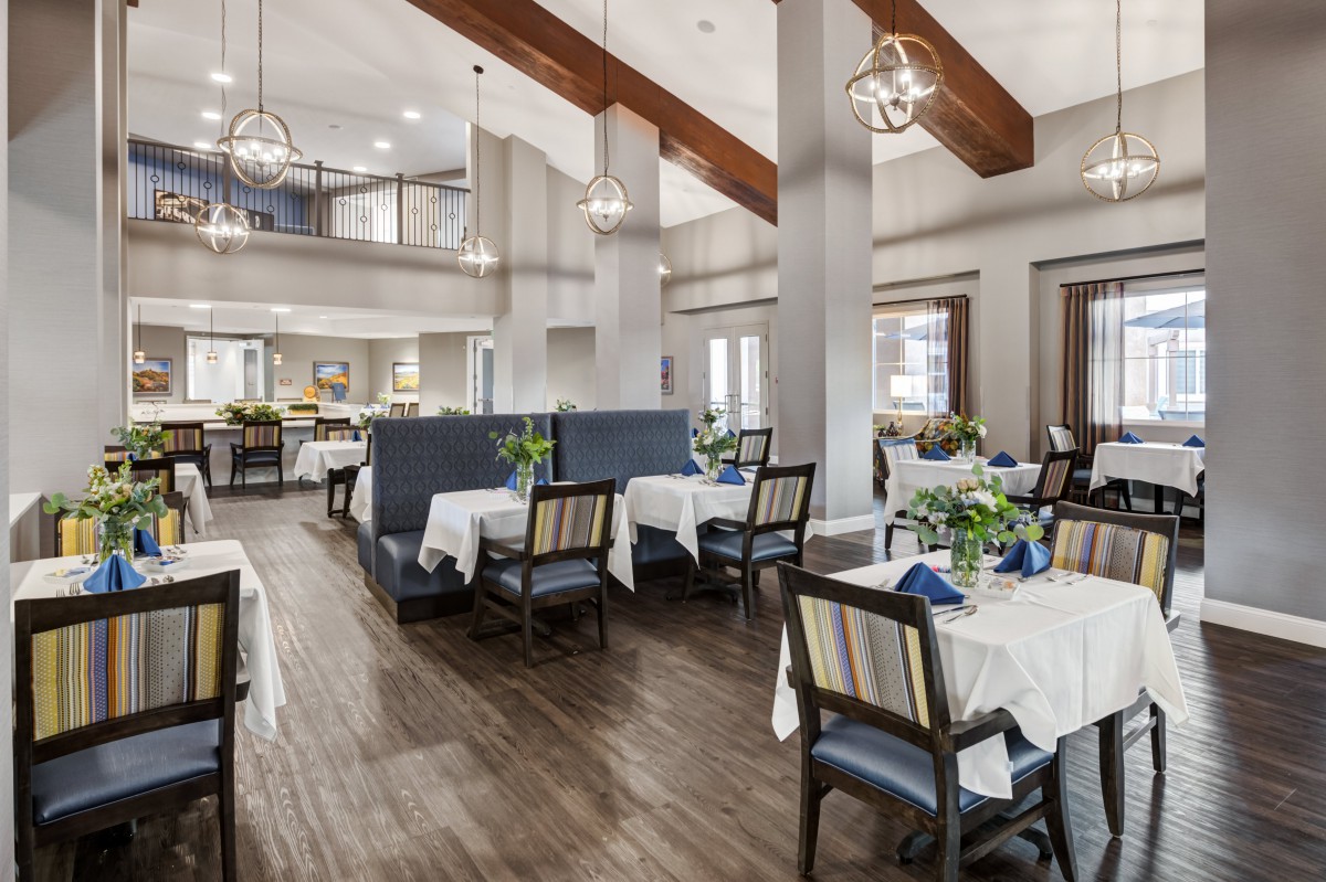 A modern restaurant interior with neatly arranged tables and chairs, featuring elegant chandeliers and high ceilings.