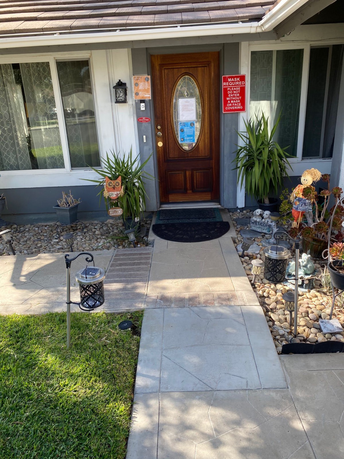 A welcoming house entrance with plants, outdoor decor, and a clear pathway leading to the wooden front door.