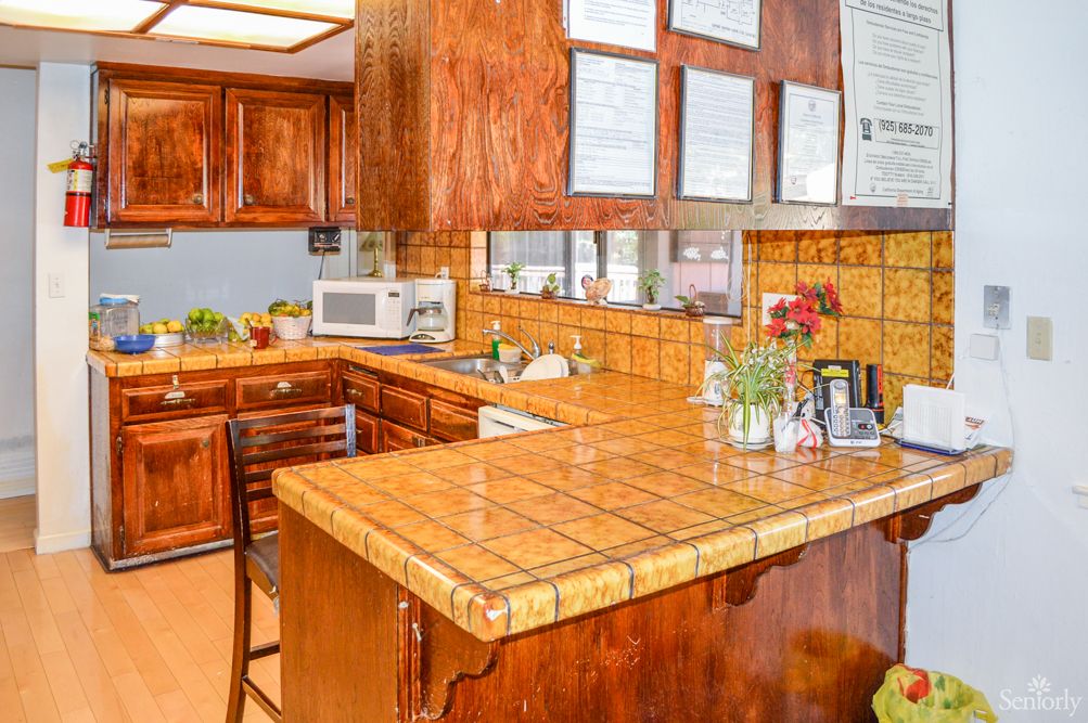 A cozy kitchen featuring wooden cabinets and a tiled countertop, complete with appliances and decorative plants.