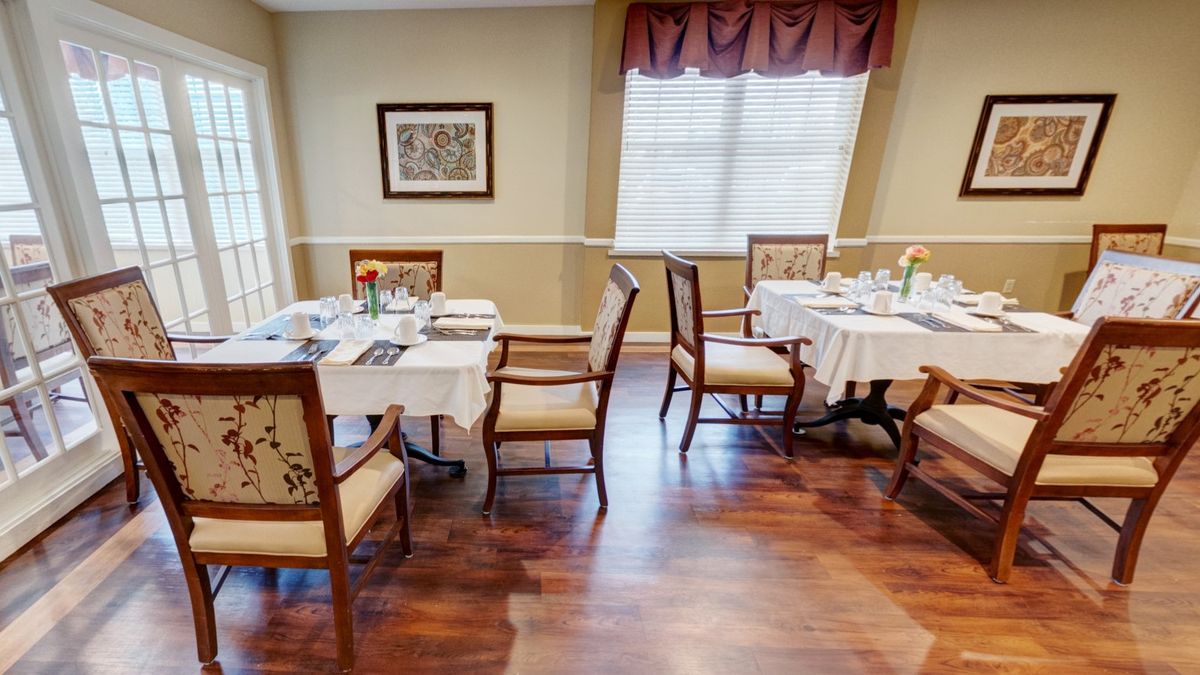 A cozy dining area with elegantly set tables and chairs, featuring hardwood floors and soft lighting.
