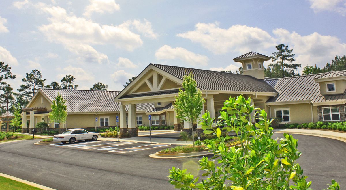 A suburban building with a parking lot and greenery on a cloudy day.