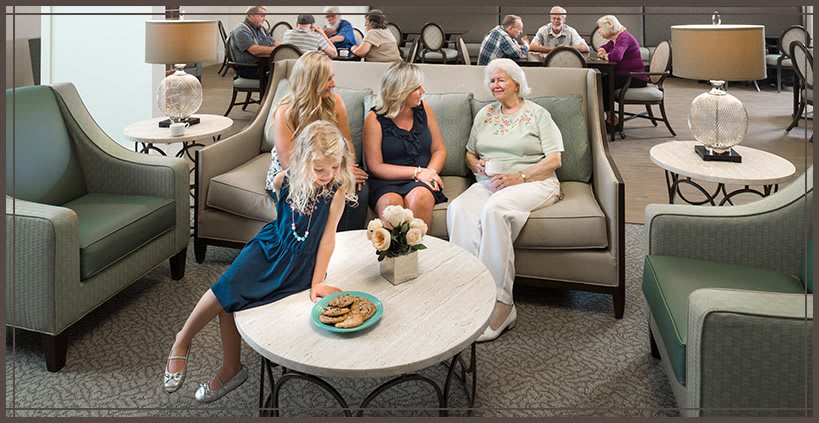 A family gathering featuring a lively conversation among several women sitting on a sofa, with cookies on the table nearby.