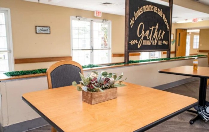 A cozy restaurant interior with a wooden table, chairs, and decorative plants.