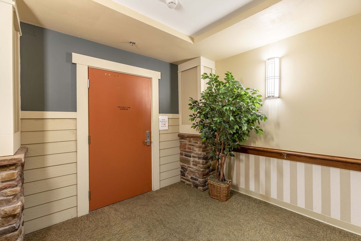 A warmly lit hallway featuring a red door, potted plant, and wall sconce.