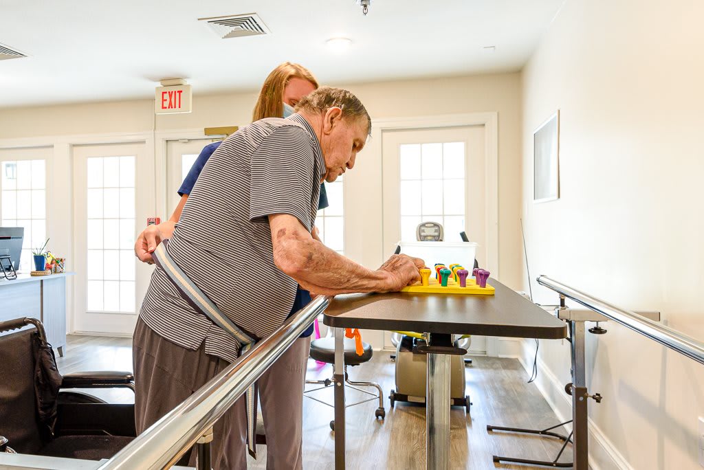 An elderly person undergoing physical therapy with the help of a caregiver.