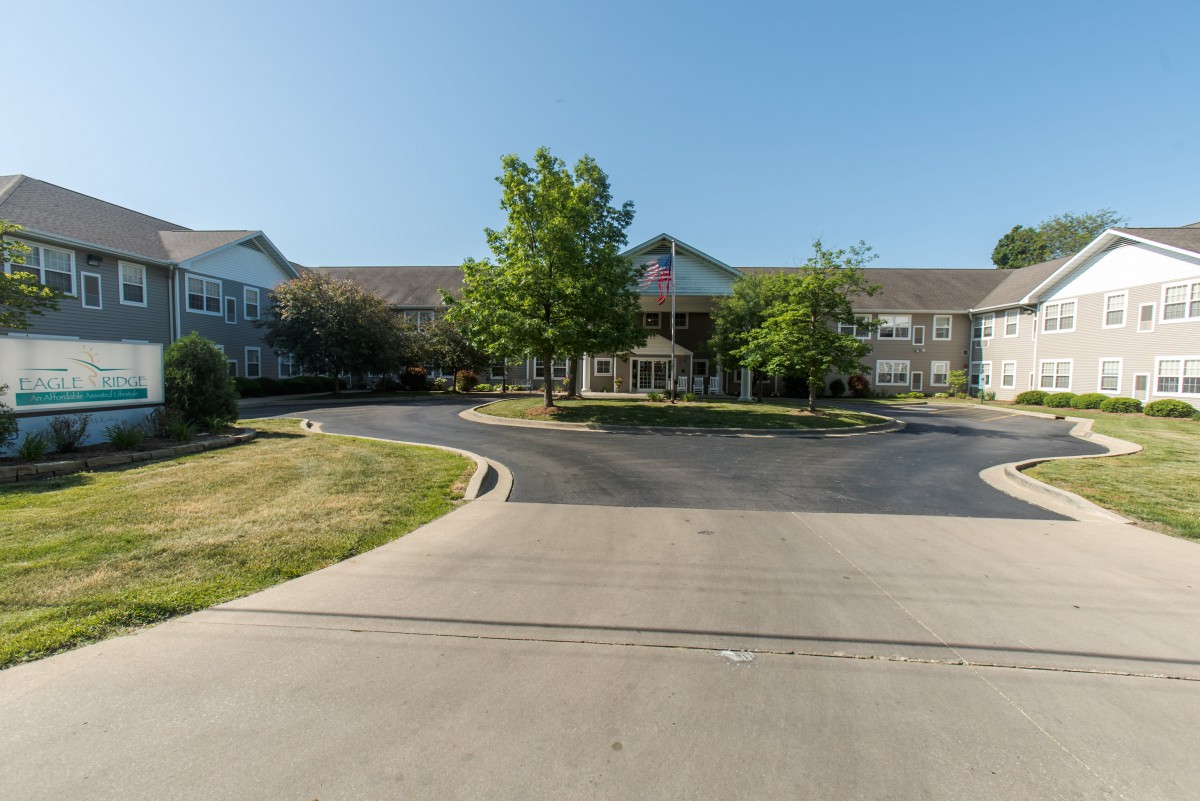 A wide view of a building with a circular driveway and surrounding greenery under a clear sky.