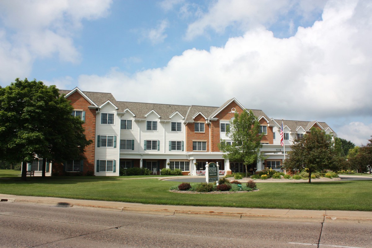 A three-story residential building with a landscaped lawn and trees.