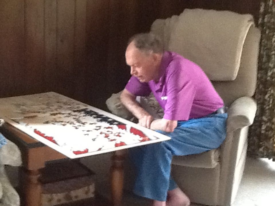 An elderly man seated and concentrating on a puzzle.