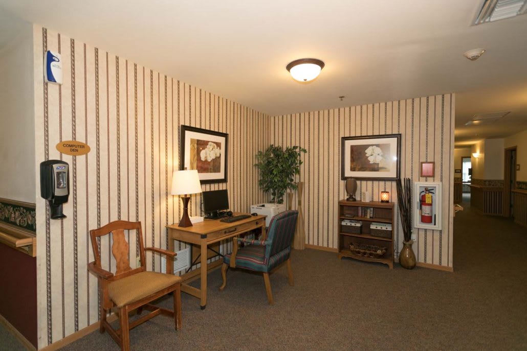 A small, cozy office space with a wooden desk and chairs, decorated with framed wall art and an indoor plant.