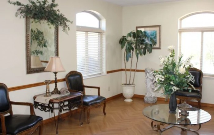 A cozy living room with a wooden chair, glass table, and decorative plants by the window.