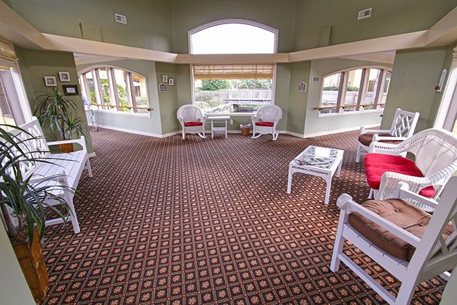 A spacious living room with large windows, wicker chairs, and a patterned carpet.