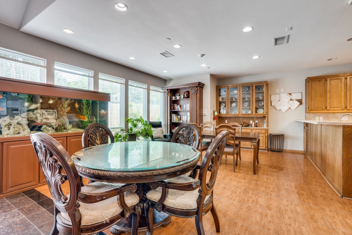 A stylish dining room with a round glass table, elegant chairs, and wooden flooring, complemented by a fish tank and decorative plants.