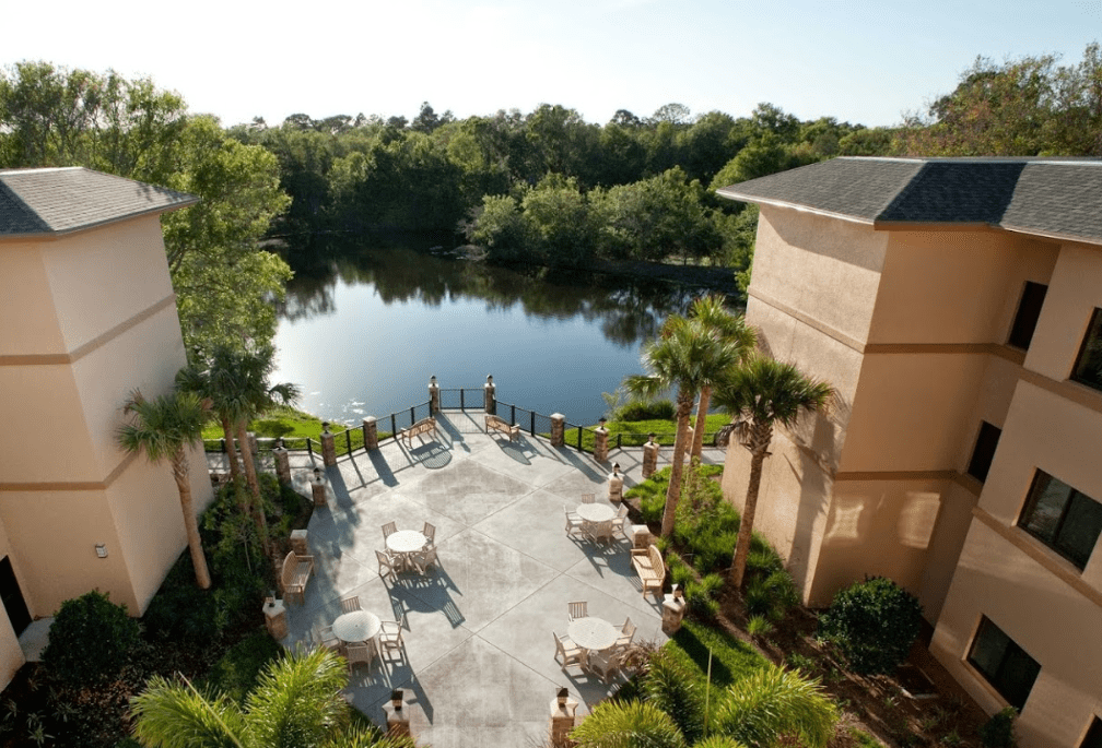 A serene view of a hotel patio overlooking a tranquil lake surrounded by lush greenery.