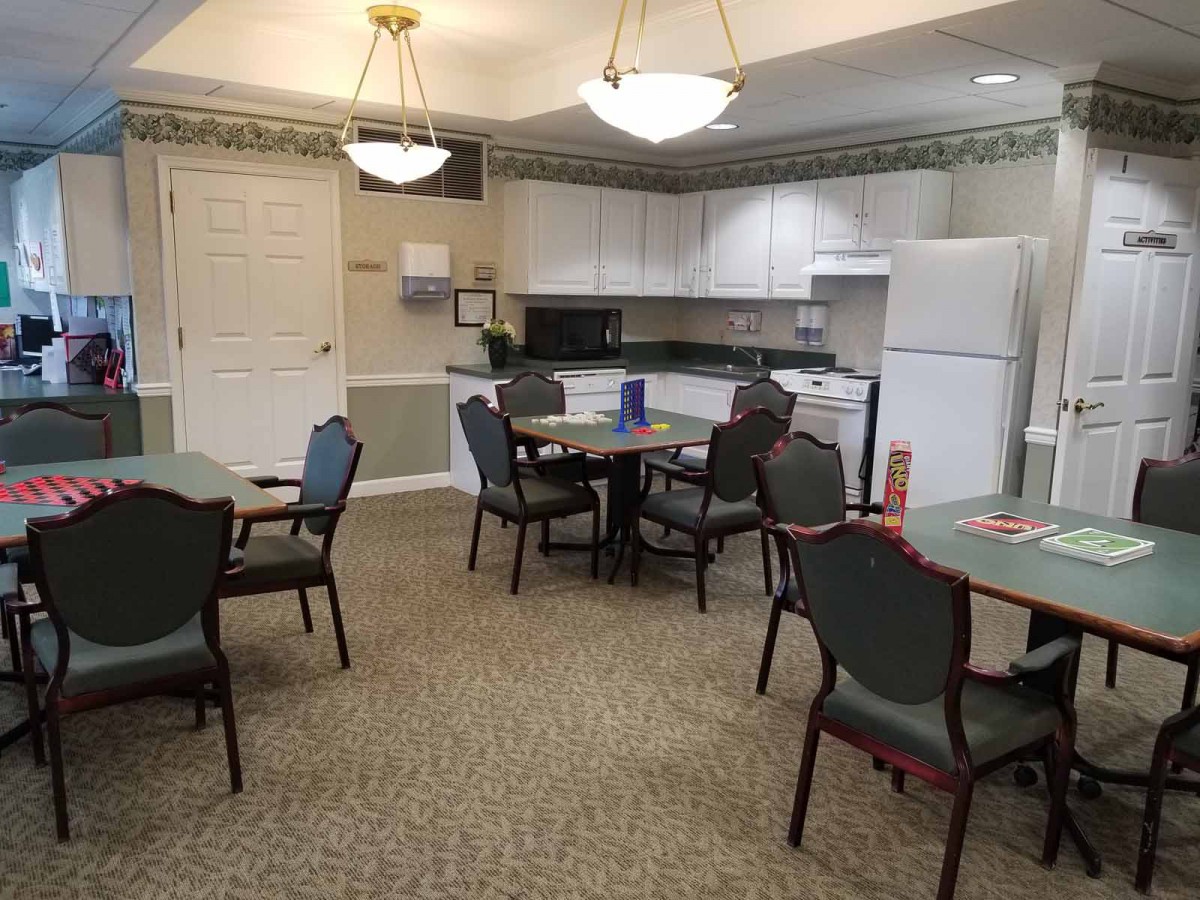 A communal kitchen area with multiple tables and chairs, equipped with appliances such as a refrigerator and microwave.
