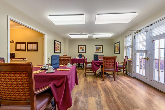 A cozy dining room with tables set for service, featuring wooden floors and artwork on the walls.